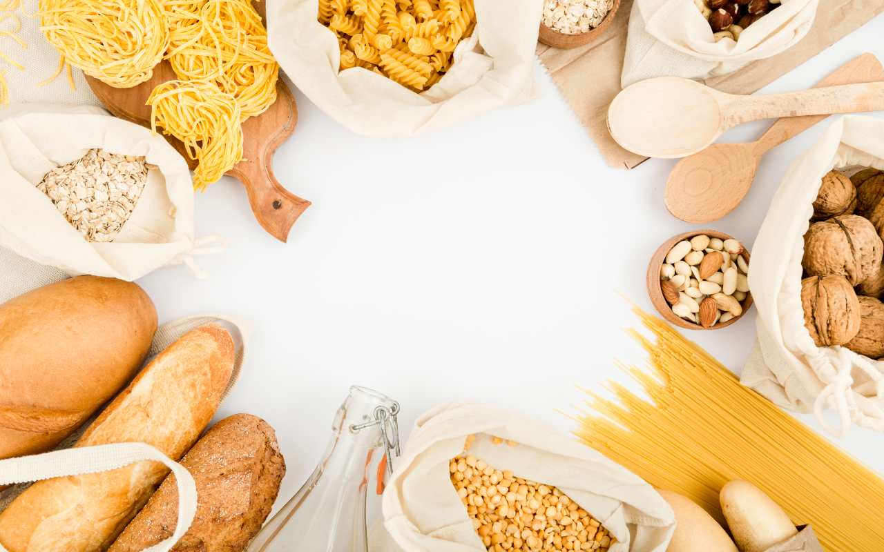 Diversi formati di pasta, legumi, cereali, frutta secca e pane su un tavolo