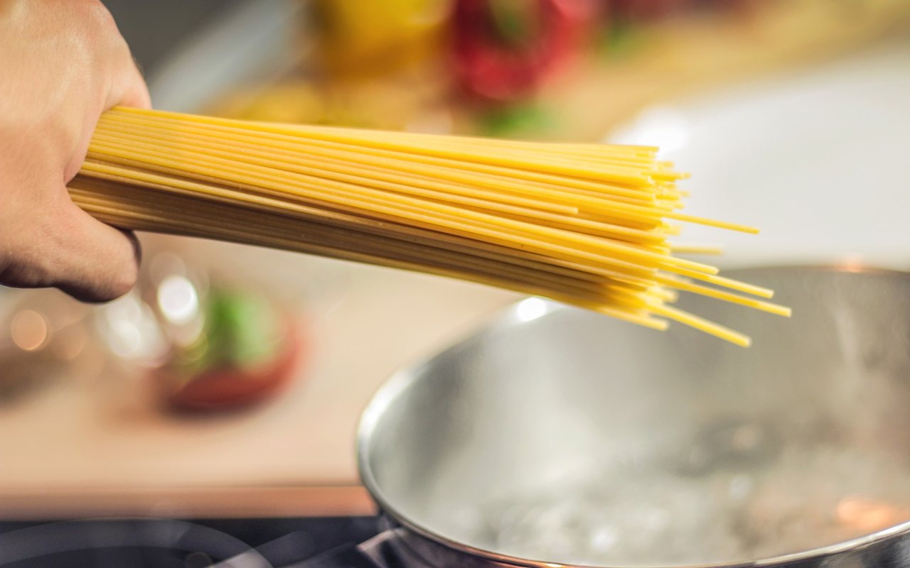 Una persona butta degli spaghetti crudi in una pentola con acqua bollente