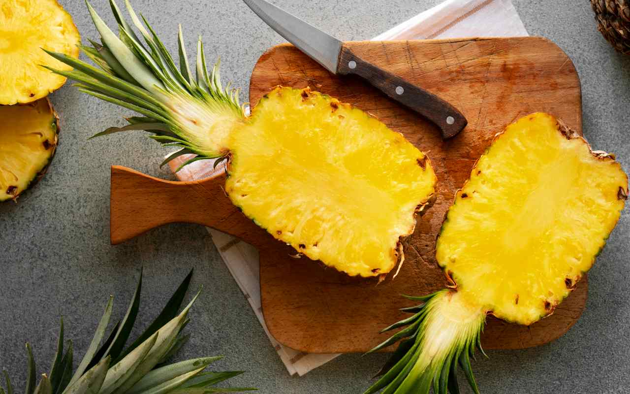 Ananas tagliata a metà su un tagliere accanto a un coltello