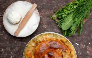 Una torta di scarola accanto a un impasto salato e verdure fresche su un tavolo